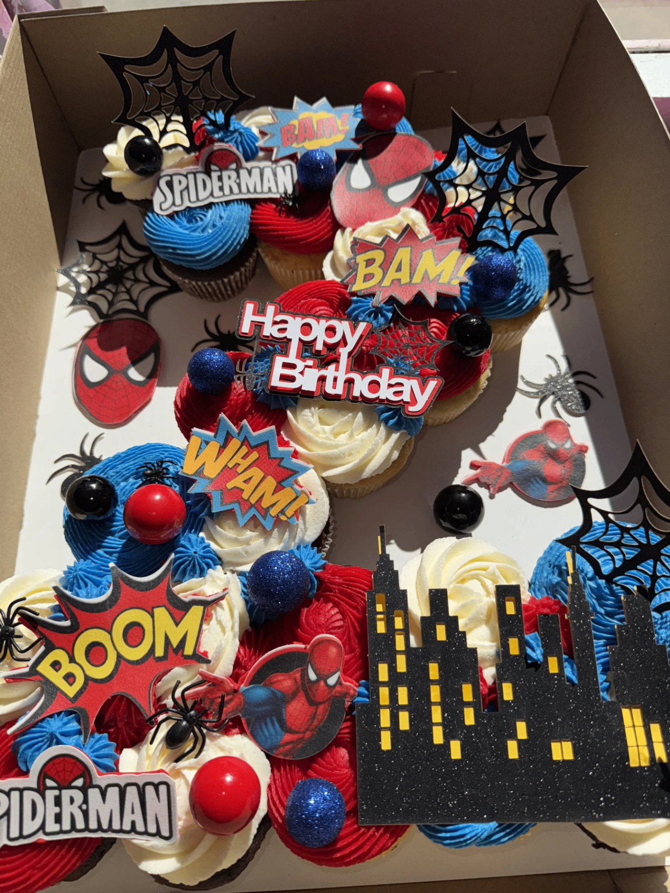 Spider-Man themed cupcake box with red and blue buttercream and comic-book toppers